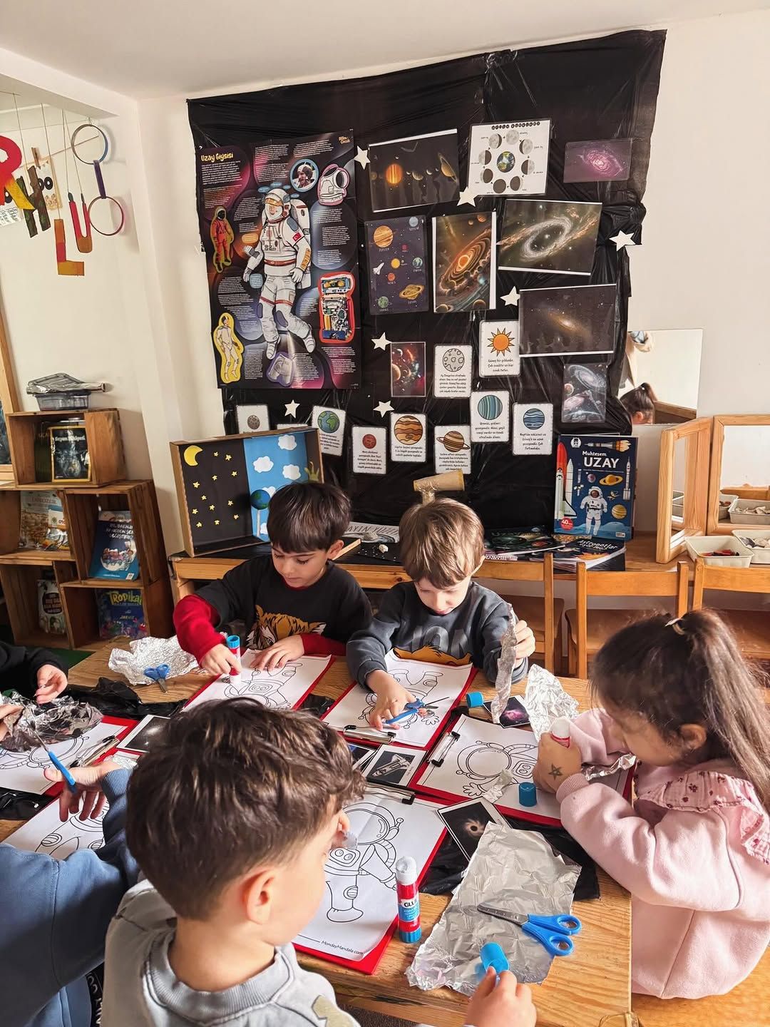 Uzay temalı kesme ve yapıştırma çalışmasında aynı masa çevresindeki çocuklar